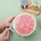 Hands stretching a silicone lid over a cut watermelon